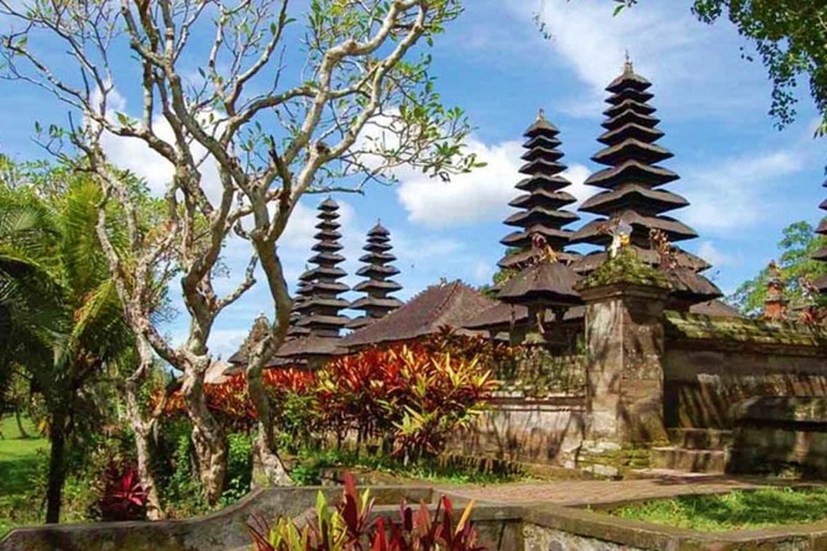 Ancient Balinese temple with tiered black pagoda roofs surrounded by lush tropical gardens and ornamental plants under blue s