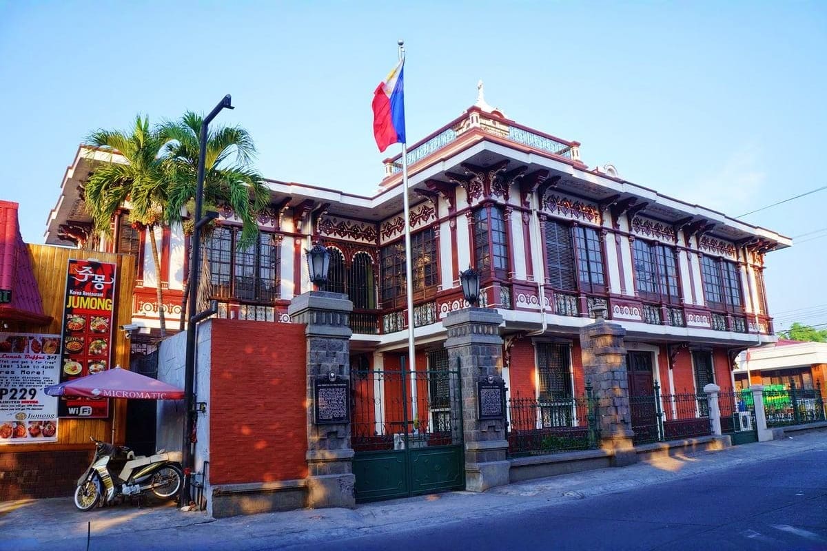 Historic Spanish colonial building with red and white facade, Philippine flag, ornate wooden balconies and stone pillars in M