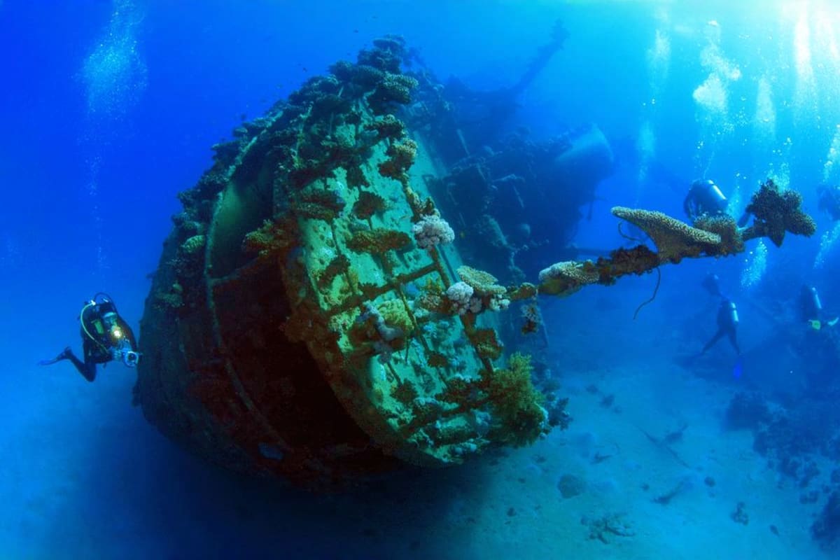 Coron Diving Tour Scuba divers exploring a sunken shipwreck covered in coral and marine growth in deep blue ocean water