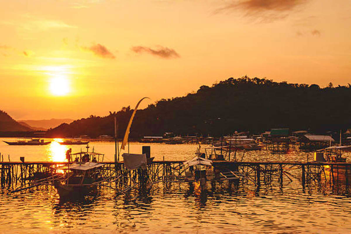 Coron Diving Tour Fishing boats and wooden docks at sunset in Coron harbor with forested hills silhouetted against golden sky
