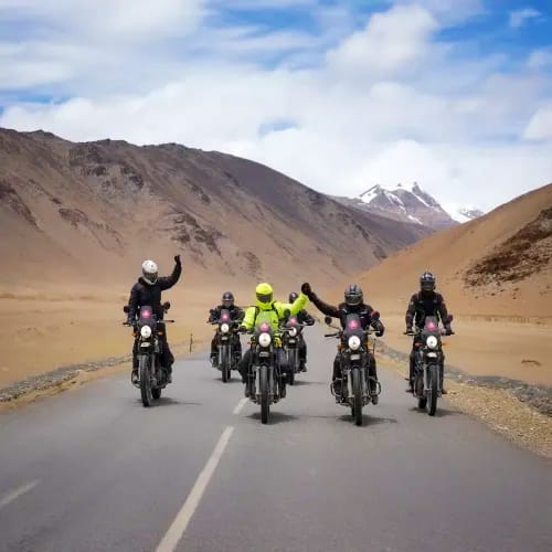 Group of motorcyclists riding on a mountain highway in Ladakh with snow-capped peaks and barren desert landscape in backgroun