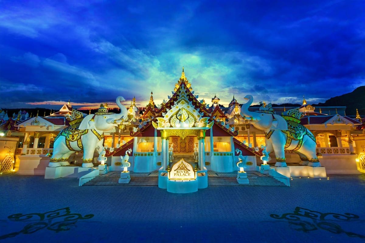 Illuminated Thai temple with golden spires and white elephant statues at twilight, featuring traditional architecture and blu