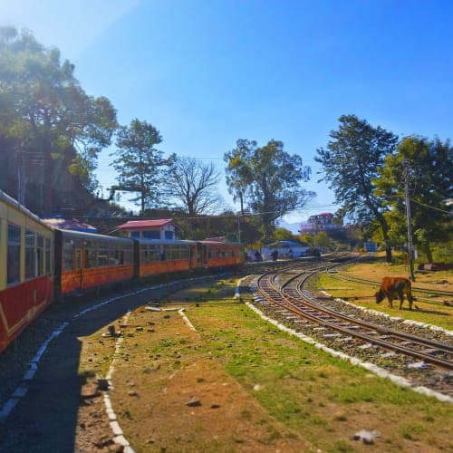Red and orange vintage train on curved railway tracks in green landscape with trees under clear blue sky