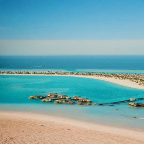 Aerial view of overwater bungalows in turquoise Red Sea waters with pristine white sand beach and coastal resort in backgroun