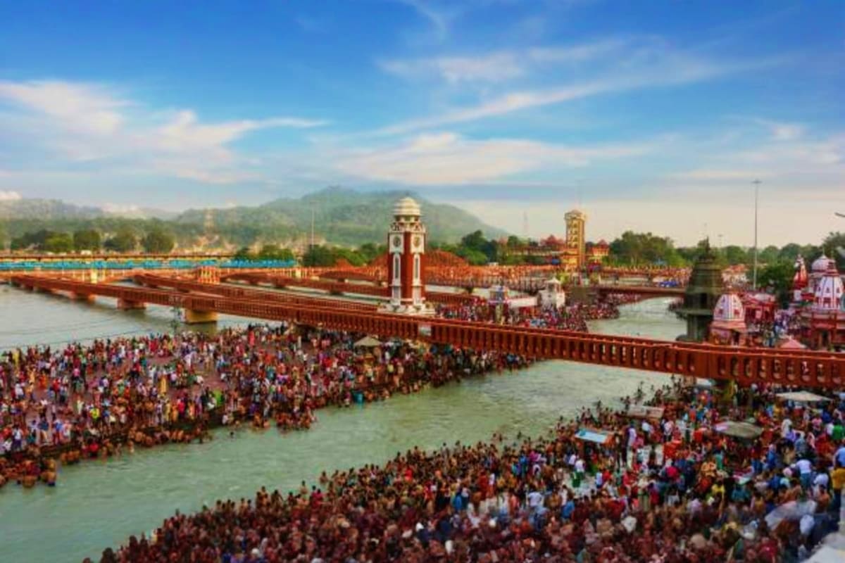 Haridwar Rishikesh Tour from Delhi A Spiritual Himalayan Escape Massive crowd of pilgrims gathered at the Ganges River in Haridwar with red fort walls, temples, and mountains in background