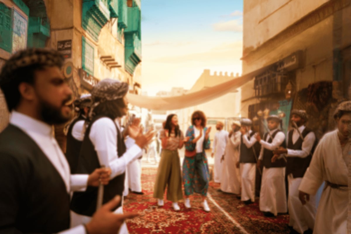 Busy market street in historic Saudi Arabian city with traditional architecture, people in traditional dress gathered on red