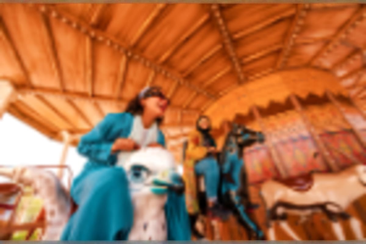 Tourists in blue clothing inside a traditional wooden-beamed structure with terracotta walls and decorated textiles in Saudi