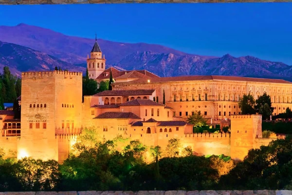Alhambra palace illuminated at dusk with snow-capped Sierra Nevada mountains in background, Granada Spain