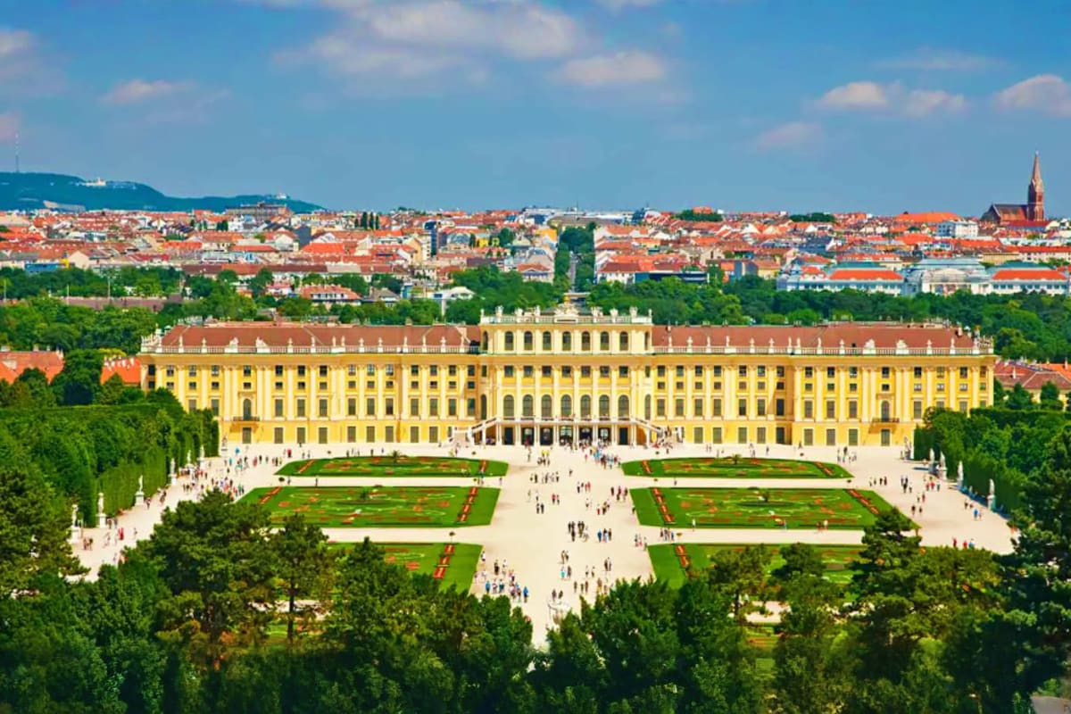 Schönbrunn Palace in Vienna with yellow baroque facade, formal gardens, and Vienna cityscape in background