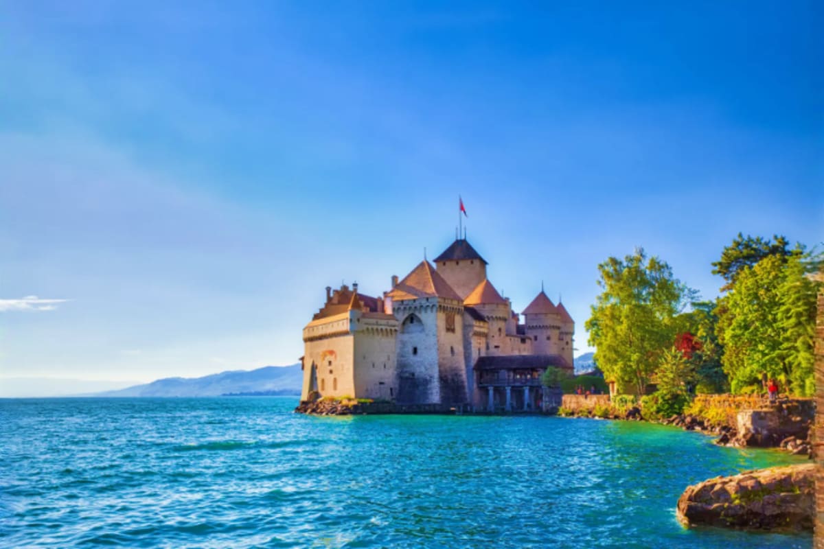Chateau de Chillon historic castle on Lake Geneva surrounded by turquoise water and Alpine mountains under clear blue sky