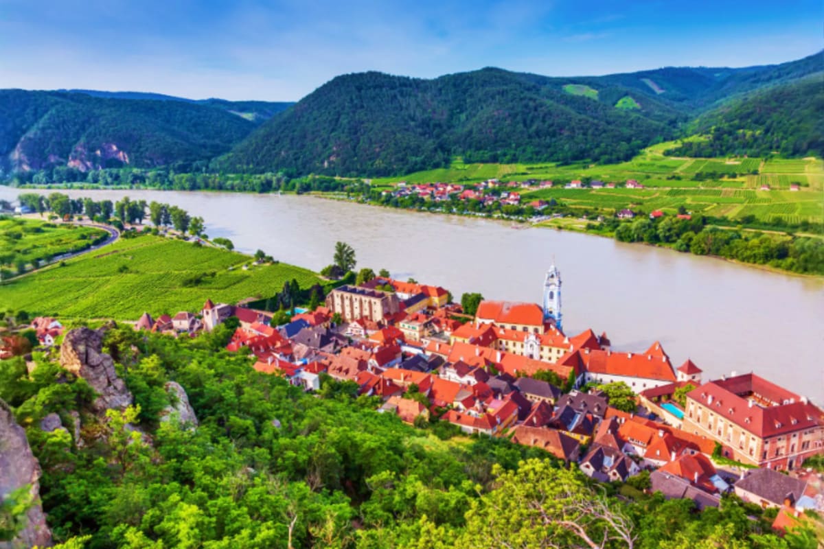 Aerial view of Dürnstein village with red-roofed buildings, blue church tower, and Danube River winding through forested Aust