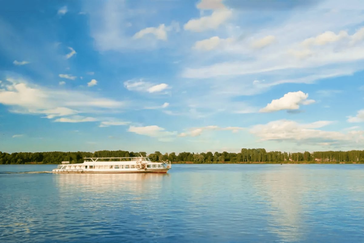 White river cruise ship sailing on calm blue water with forested shoreline and white clouds in sky
