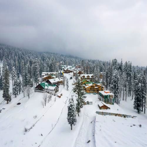 Aerial view of snow-covered resort nestled among frosted pine forests with ski slopes and wooden lodges during winter in Kash