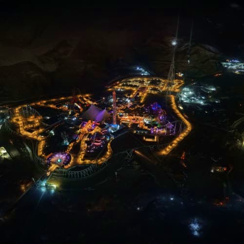 Aerial nighttime view of illuminated theme park with golden and purple lights outlining pathways and attractions against dark