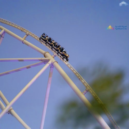 Roller coaster ride with passengers on track against blue sky at amusement park