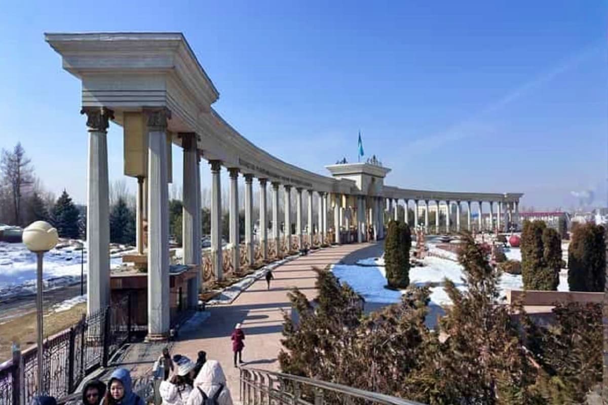 Grand colonnade with classical columns and turquoise dome in Almaty, featuring cypress trees and snow-covered grounds under c