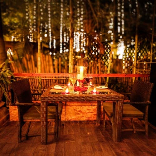 Candlelit outdoor dining table for two with hanging string lights in warm golden ambiance at night