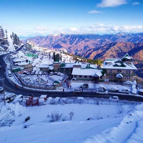 Snow-covered mountain resort town with hotels and buildings nestled in valley surrounded by snow-capped Himalayan peaks under