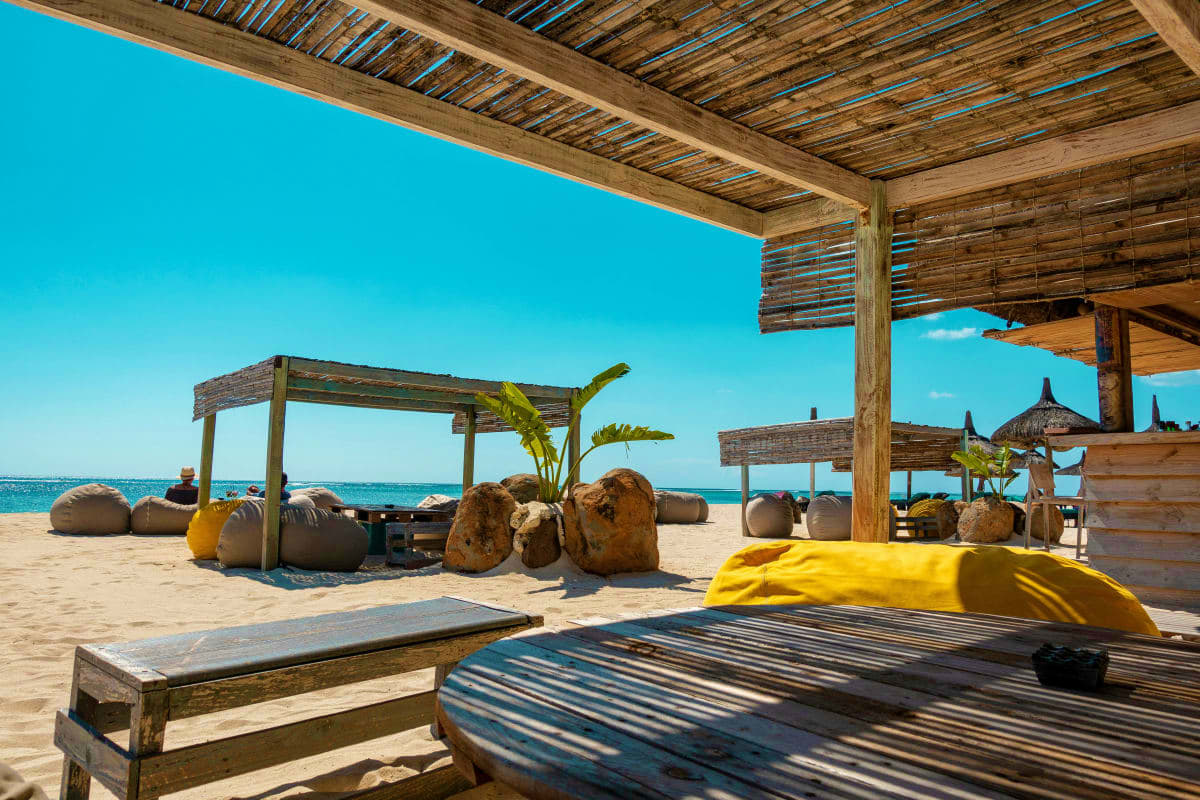 Beachfront wooden pergola structures with loungers and bean bags overlooking turquoise ocean and sandy beach in Mauritius