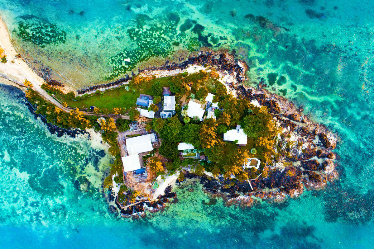Mauritius Coral Paradise Aerial view of a small tropical island with white houses, green vegetation, and turquoise coral reef waters surrounding rocky