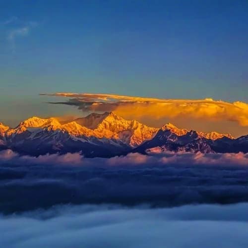 Snow-capped Himalayan mountain peaks glowing golden at sunrise above a sea of clouds in Sikkim region