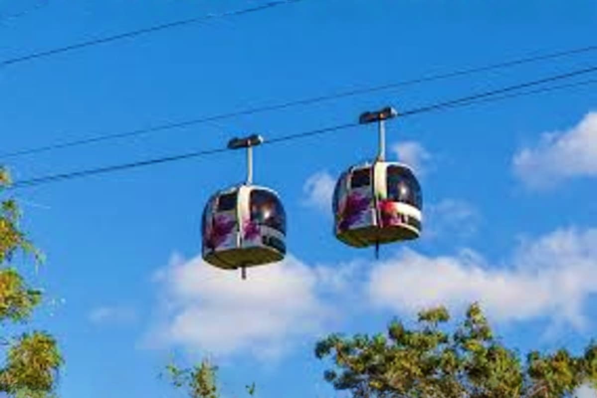 Two cable car cabins suspended on overhead wires against blue sky with white clouds and green trees below