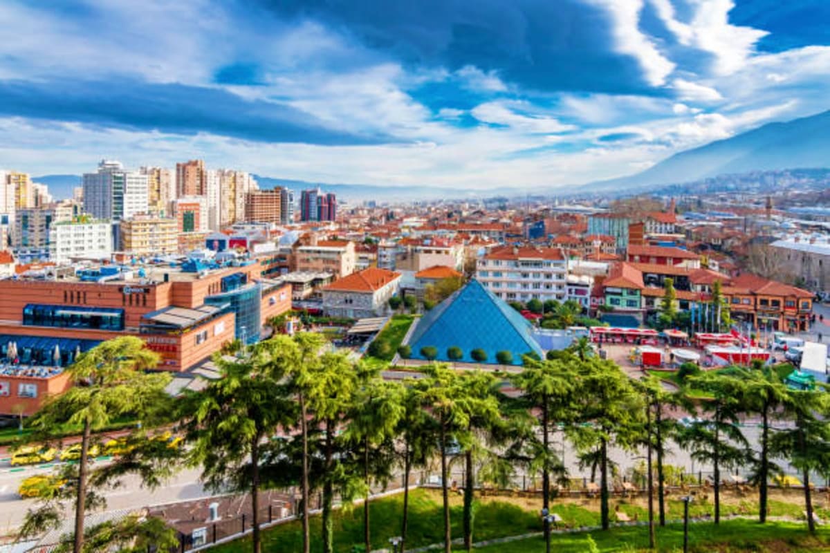 Elevated view of a Colombian city skyline with modern buildings, green parks, and mountains in the distance under a blue sky 