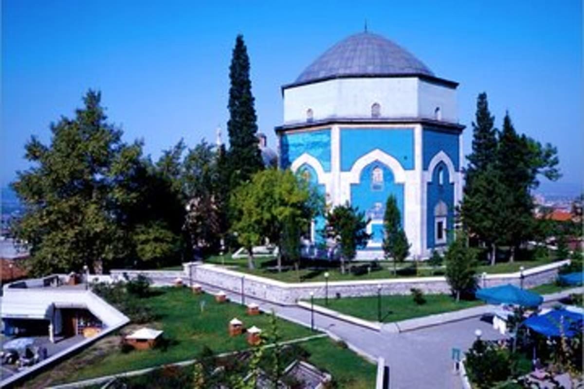Blue and white mosque with domed roof surrounded by cypress trees and manicured gardens in Turkey