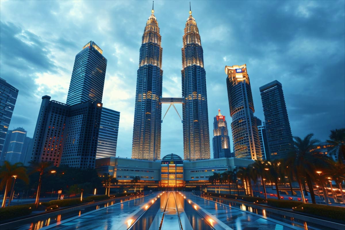 Petronas Twin Towers illuminated at dusk with surrounding Kuala Lumpur skyline and wet plaza reflecting lights