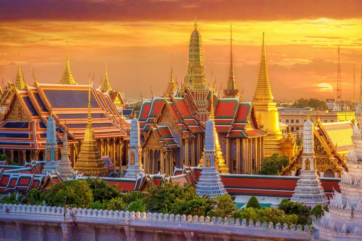 Classic Bangkok and Pattaya Holidays Grand Palace in Bangkok at sunset with golden spires, red-roofed temples, and ornate Thai architecture reflected in water