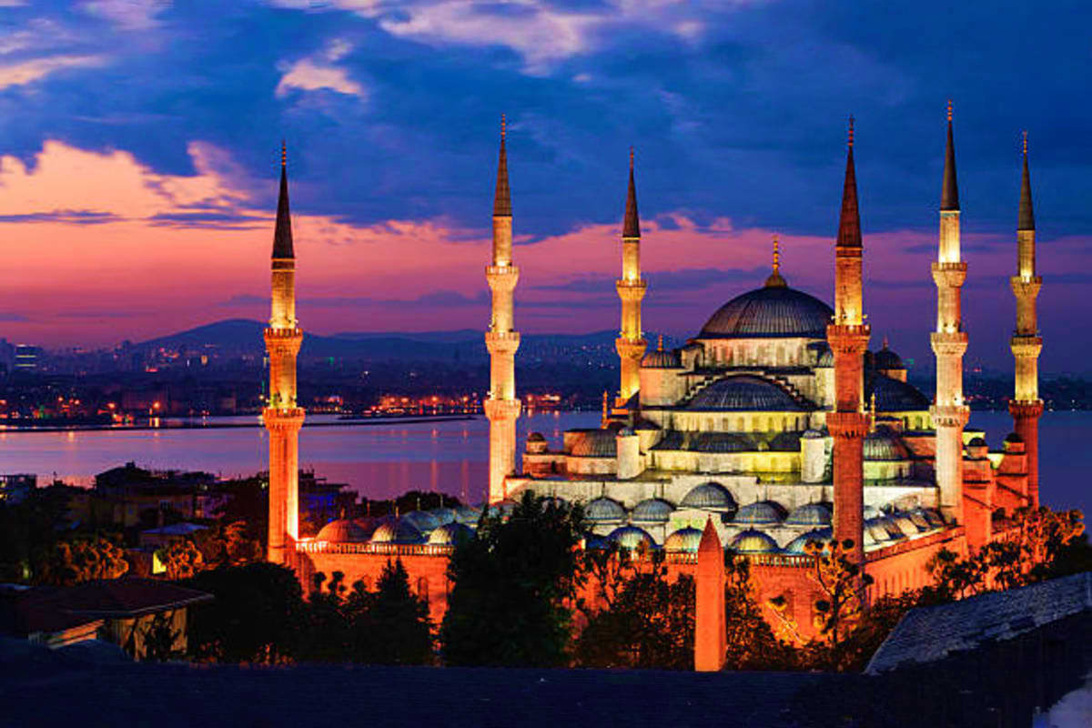 Blue Mosque in Istanbul illuminated at dusk with six minarets, domed structures, and Golden Horn waterway in background under