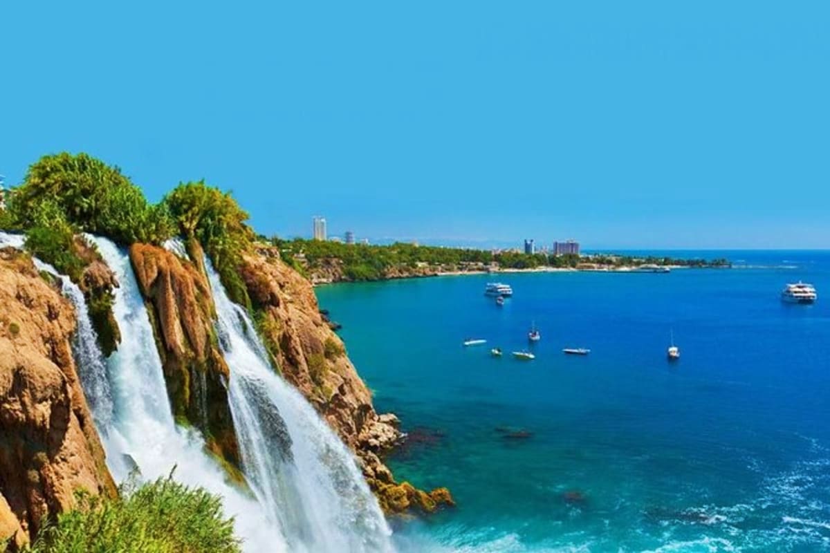 Duden Waterfall cascading into turquoise Mediterranean Sea with boats and coastal city skyline in Antalya, Turkey