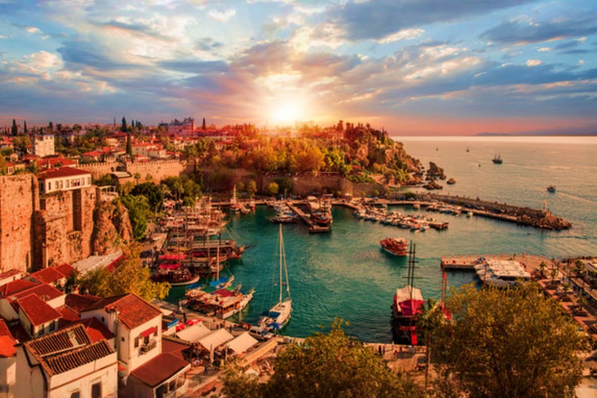 Aerial view of Antalya's old harbor at sunset with historic fortified walls, traditional boats, and Mediterranean coastline