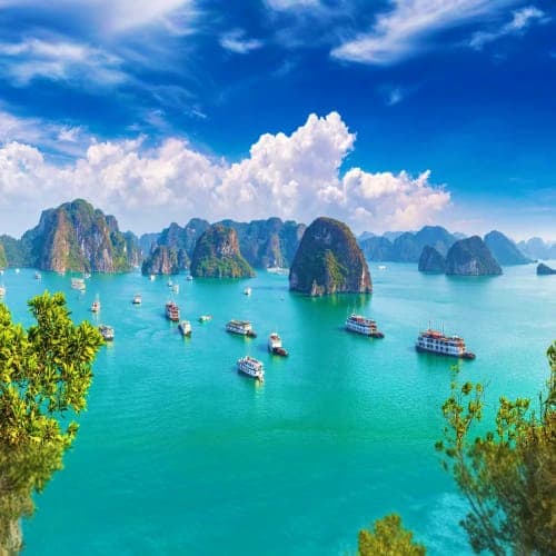 Halong Bay limestone karsts with turquoise water and traditional boats under blue sky with white clouds