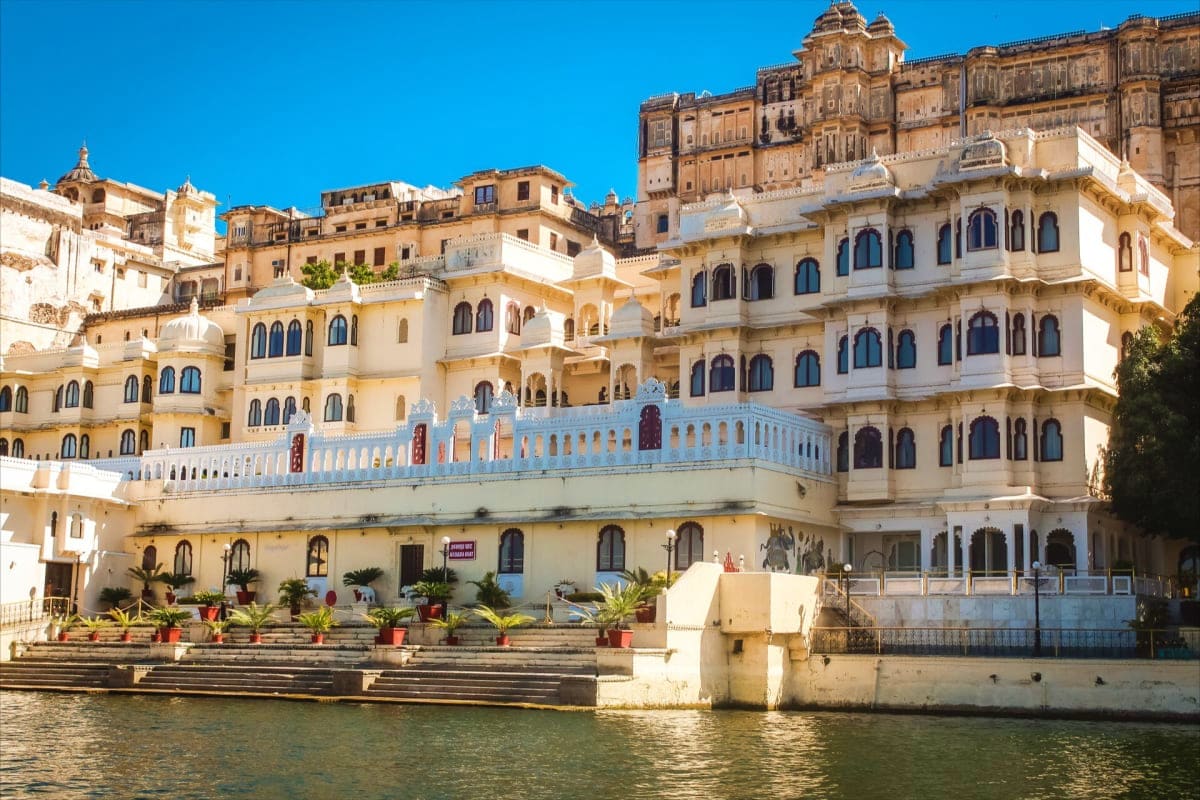 Historic lakeside palace with cream and white ornate architecture featuring blue-trimmed balconies overlooking water in Udaip