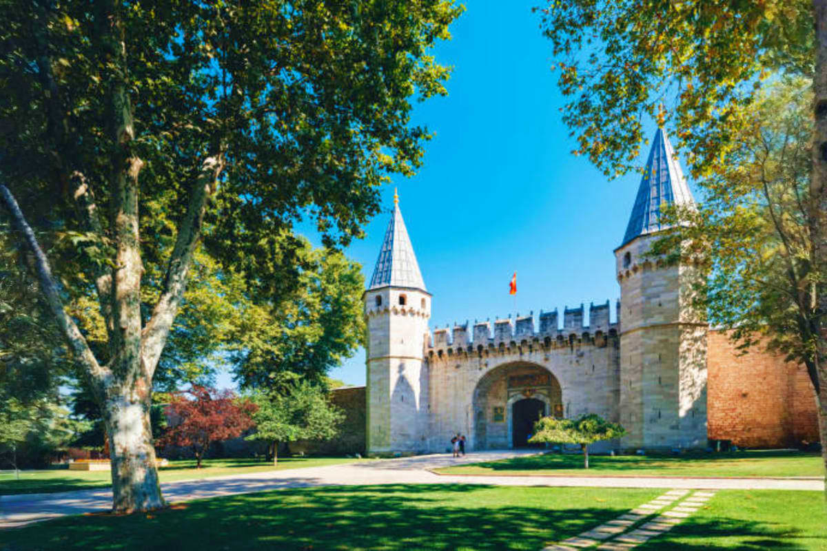 Topkapi Palace gates and towers in Istanbul with large trees and clear blue sky, historic Ottoman architecture landmark