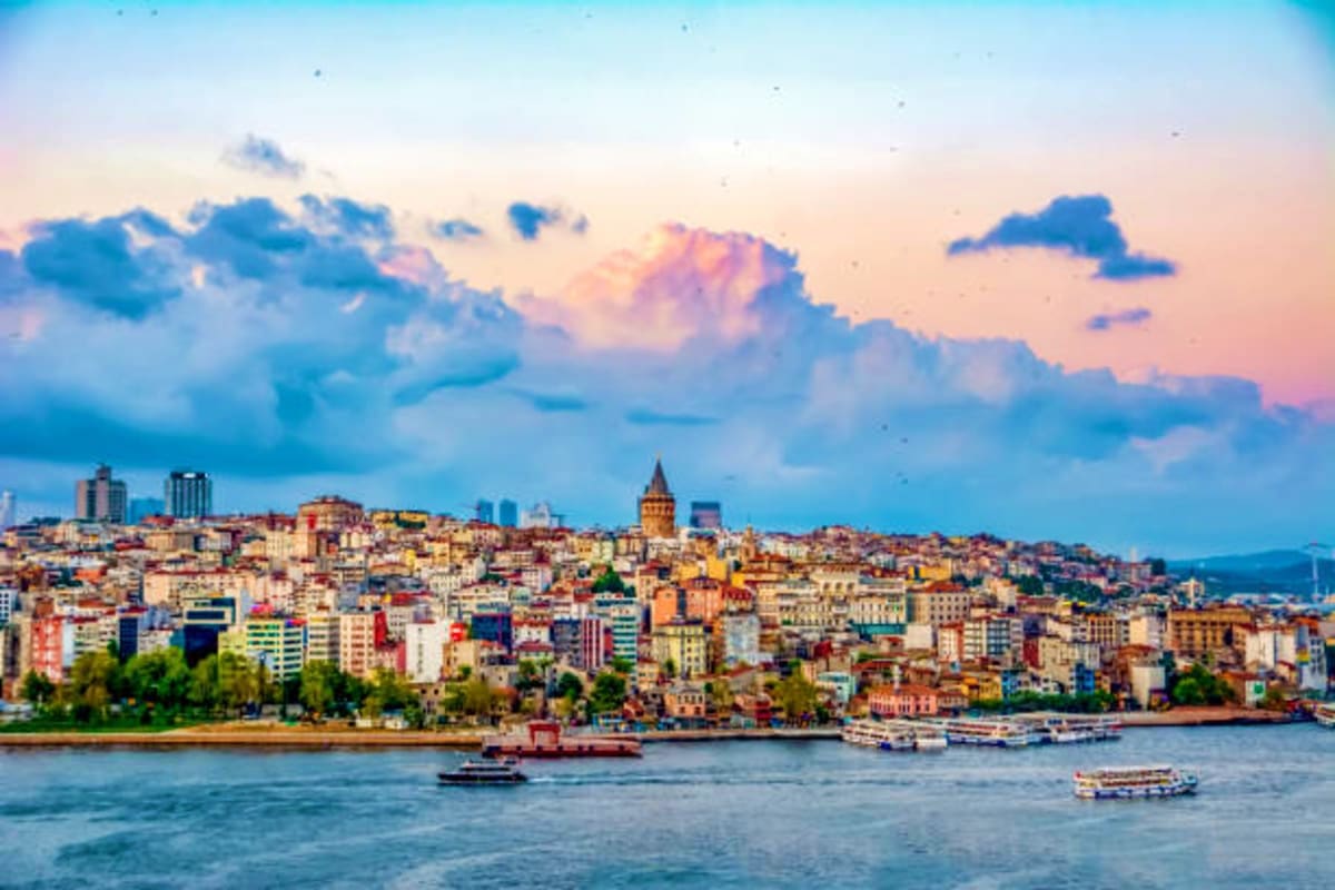 Istanbul skyline at sunset with Galata Tower, colorful buildings on hillside, and boats on Golden Horn waterway