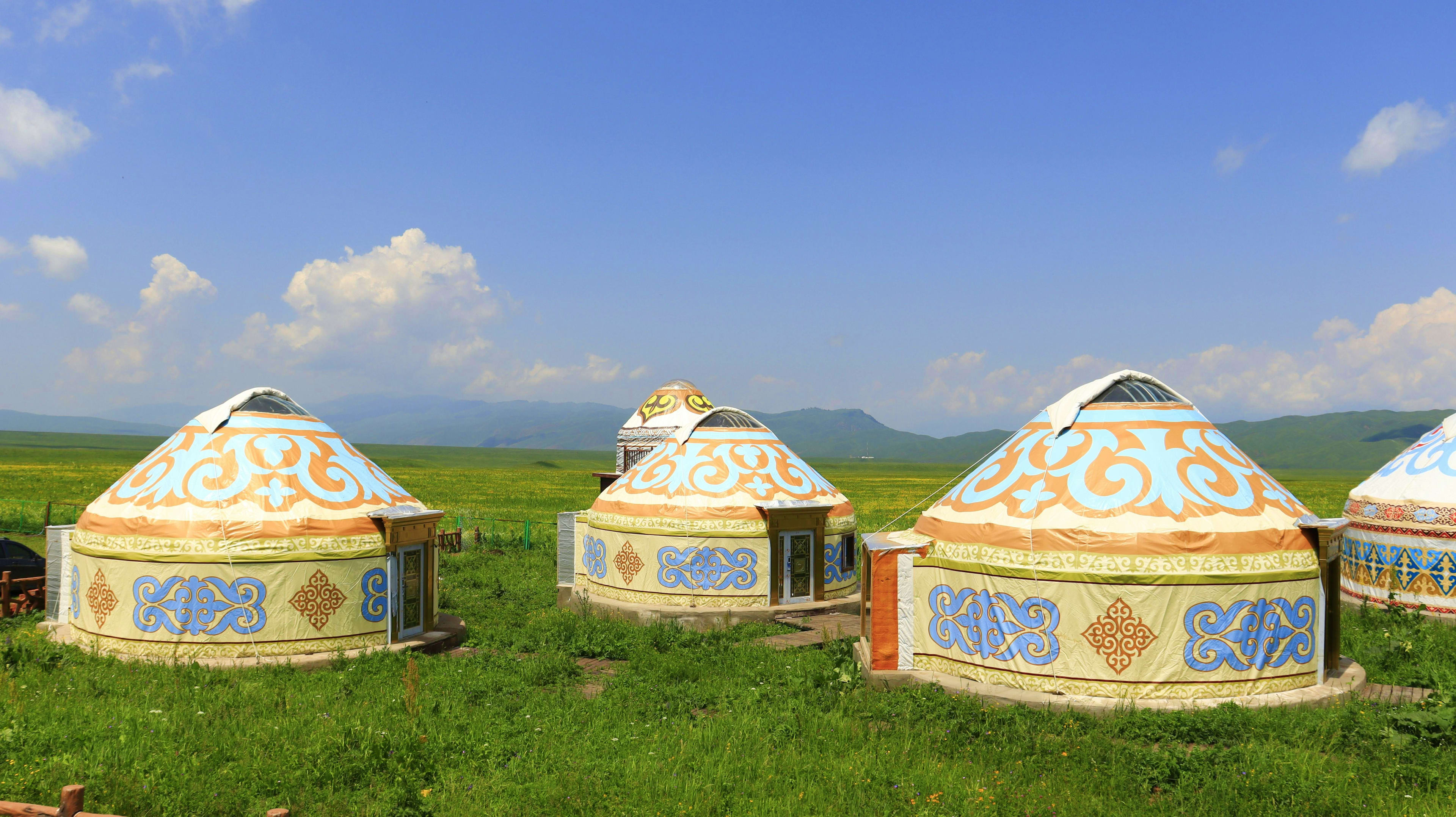 Traditional yurts with ornate blue and orange patterns on green steppe landscape with mountains in Kyrgyzstan