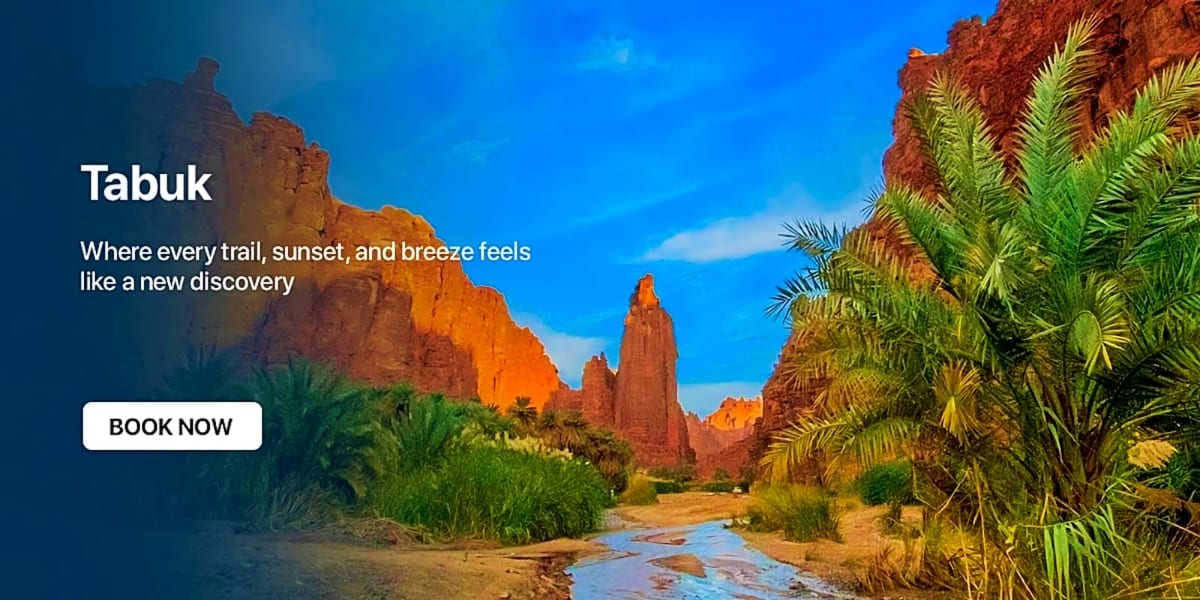 Tabuk desert landscape with red rock formations, palm trees, and a small stream under blue sky
