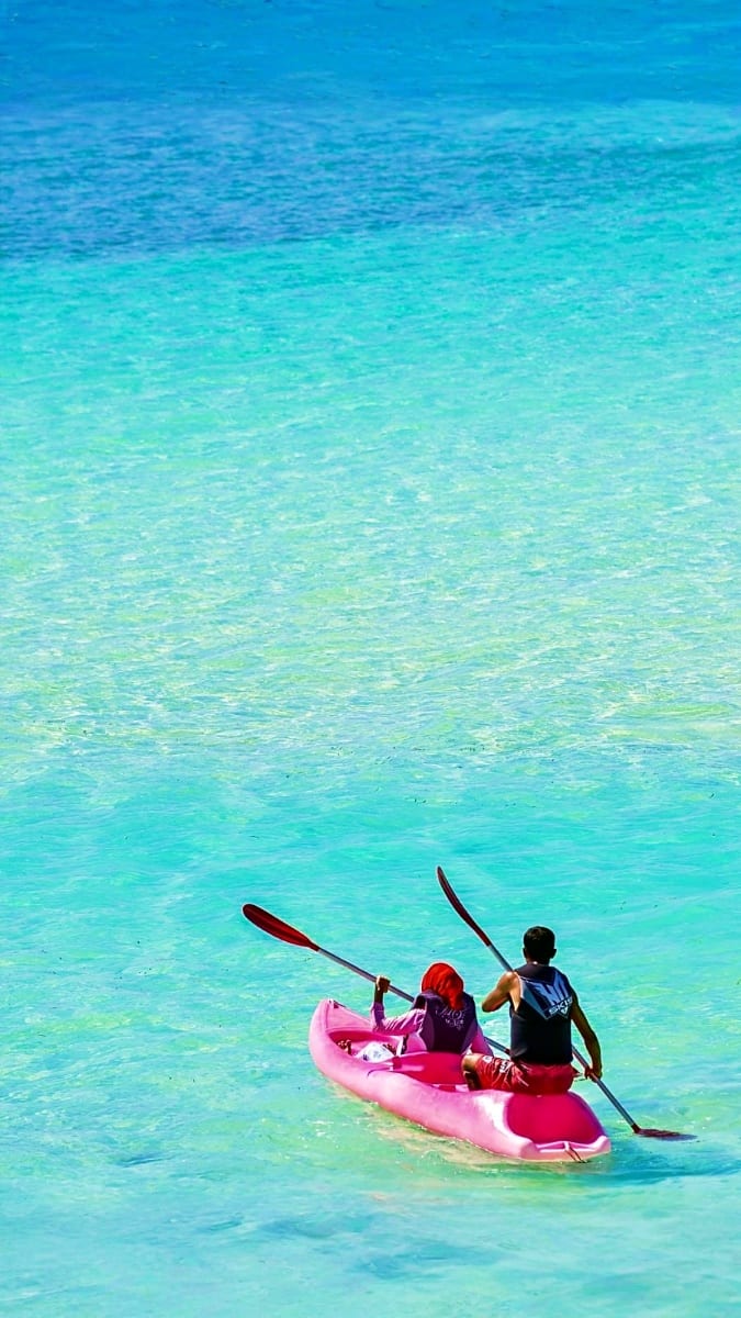 Two people kayaking in a pink transparent kayak in crystal clear turquoise water at Boracay beach