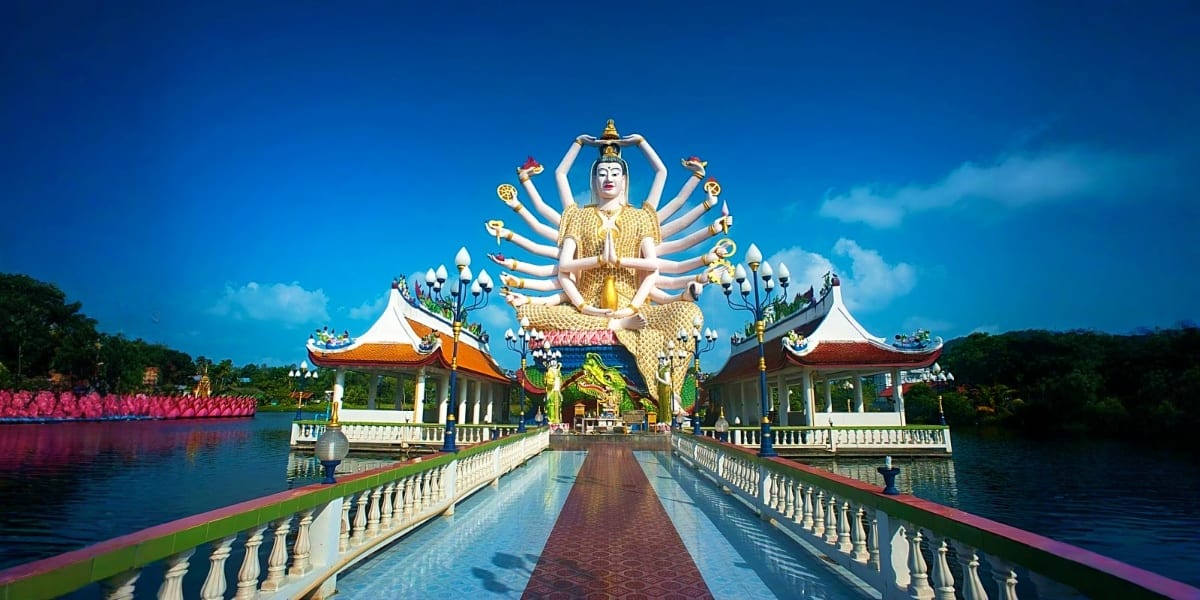 Multi-armed golden Buddha statue at Wat Plai Laem temple in Koh Samui, Thailand with blue sky and traditional architecture