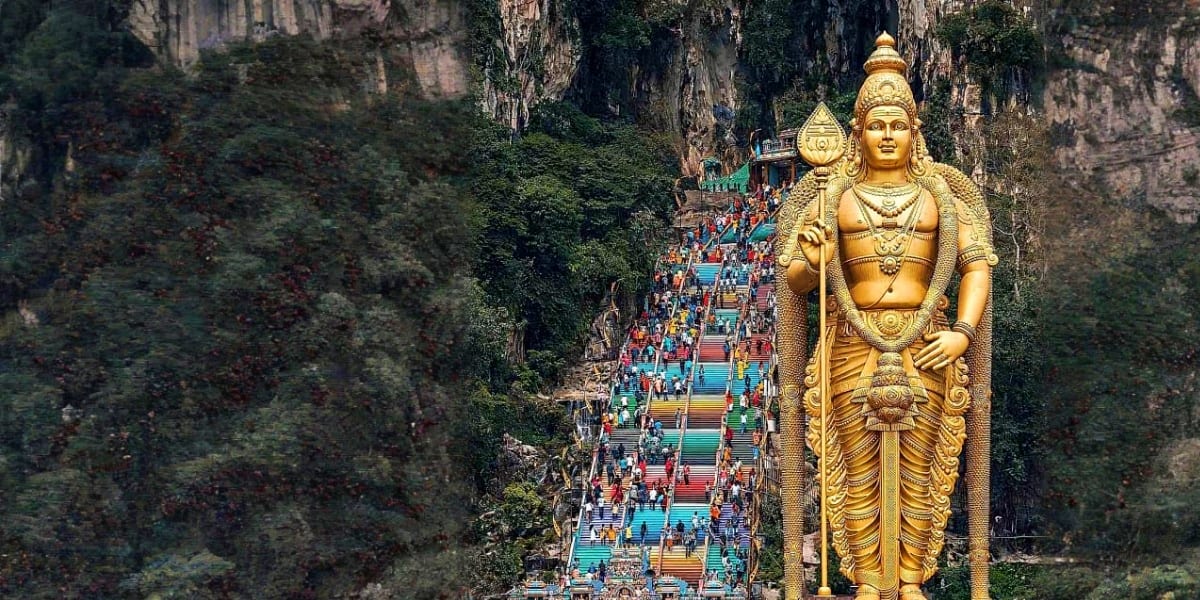 Golden Lord Murugan statue at Batu Caves entrance with colorful staircase and visitors climbing between limestone cliffs
