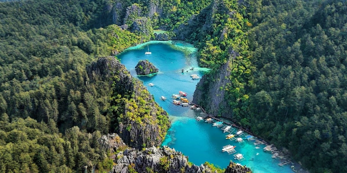Aerial view of Kayangan Lake in Coron, Philippines, surrounded by limestone cliffs and dense forest with boats in turquoise w