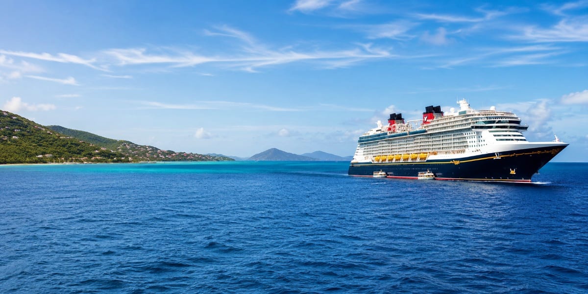 Large Disney cruise ship anchored in turquoise Caribbean waters with volcanic islands and green hillside coastline in backgro