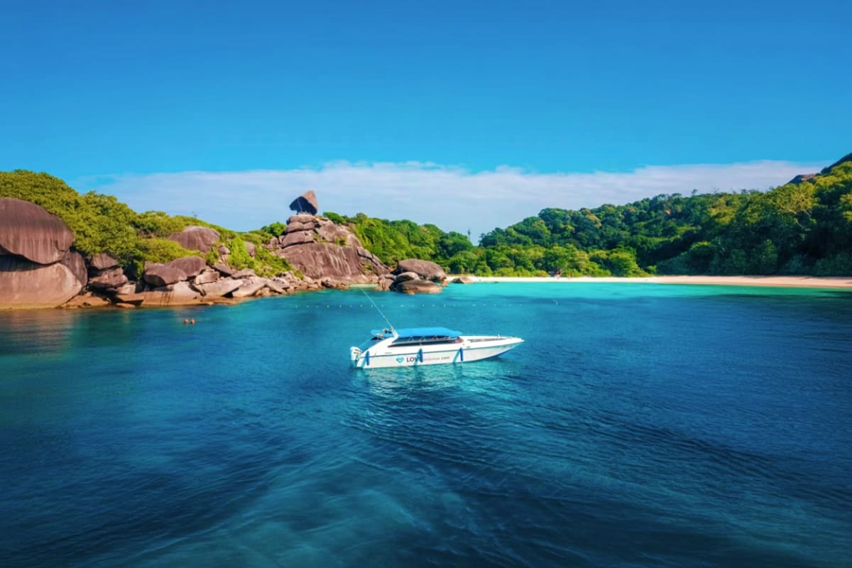 04 Island Tour on Speed Boat White speedboat anchored in turquoise water near rocky granite cliffs and white sand beach with lush green tropical forest