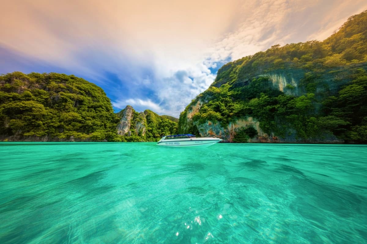 04 Island Tour on Speed Boat Speed boat anchored in turquoise water surrounded by limestone cliffs and lush tropical vegetation