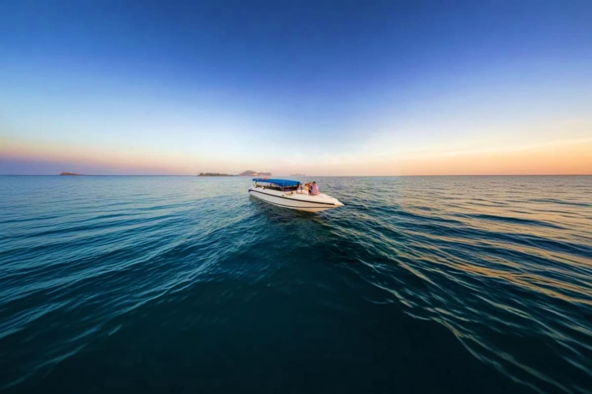 04 Island Tour on Speed Boat Speedboat with blue canopy anchored in calm turquoise water at sunset with distant islands on horizon