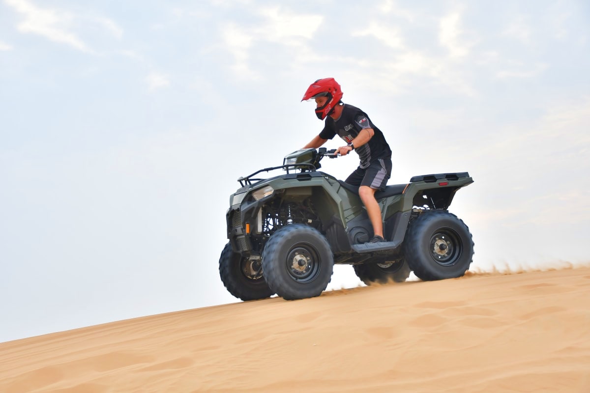 Premium Adventure with Balloon Flights Person riding ATV on sandy desert dune wearing red helmet and black shirt against cloudy sky