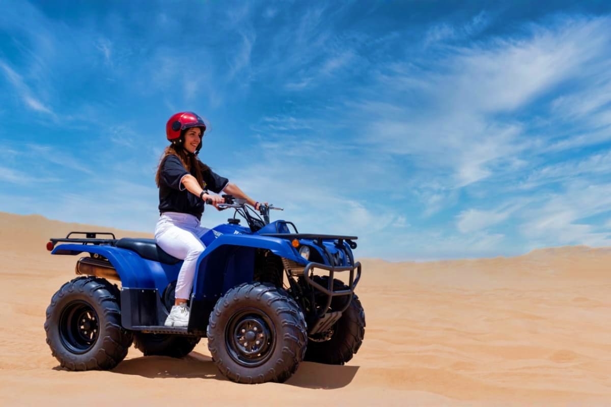 Premium Adventure with Balloon Flights Woman wearing red helmet riding blue ATV across sandy desert under clear blue sky