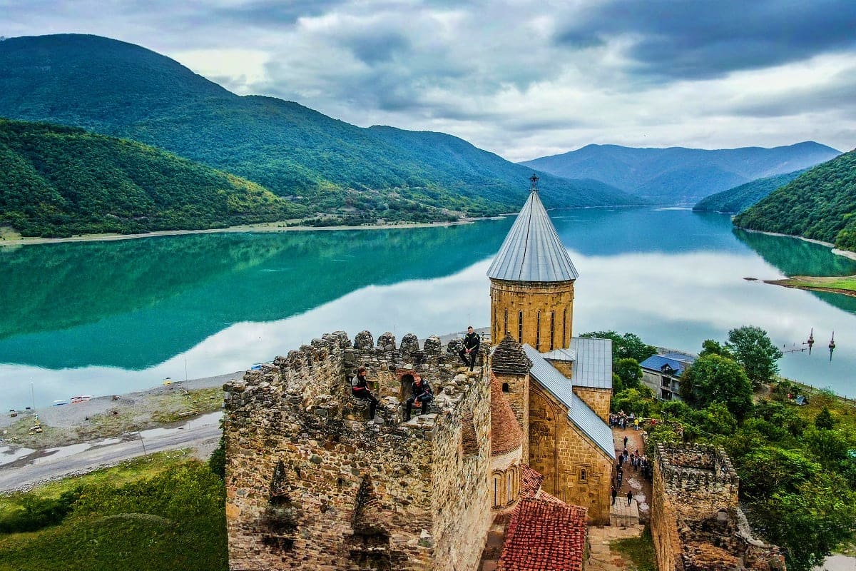 Ananuri Castle with turret overlooking turquoise Jinvali Lake surrounded by green forested mountains in Georgia